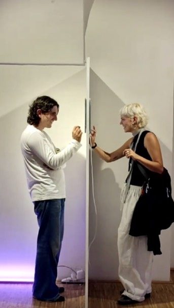 Two visitors texting through a narrow wall-mounted screen during the In Between Us installation.