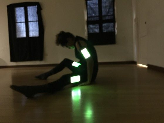A performer on the floor of a studio with glowing phones strapped to their body during the OnChange() residency.